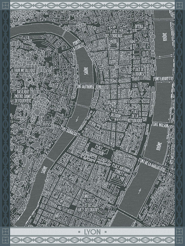 A dark gray and white street map print of Lyon, France, on a cotton dishtowel featuring labeled landmarks, rivers, and roads, framed by a decorative border with the word 'LYON' at the bottom.