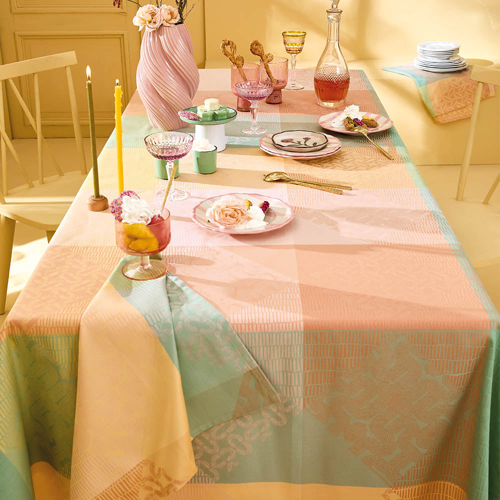 Mille Empreintes Pastel Jacquard Tablecloth in pastel cotton with geometric and plaid motifs, styled on a dining table with candles and pink glassware.
