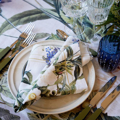Table setting with floral napkin, plates, cutlery, and glasses on a patterned tablecloth.