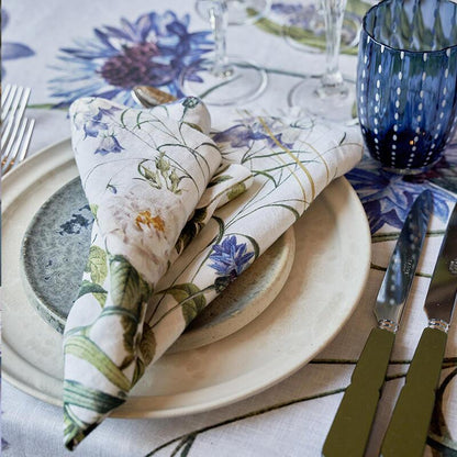 Table setting with a folded Blue Flower Garden linen napkin on a plate, and cutlery on a matching tablecloth.
