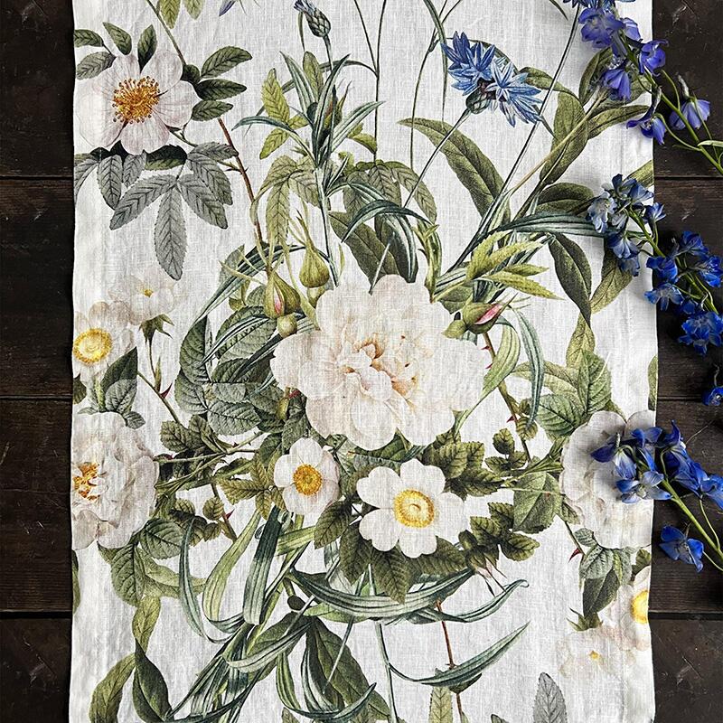 A closeup of the Blue Flower Garden table runner with white and blue flowers and green leaves
