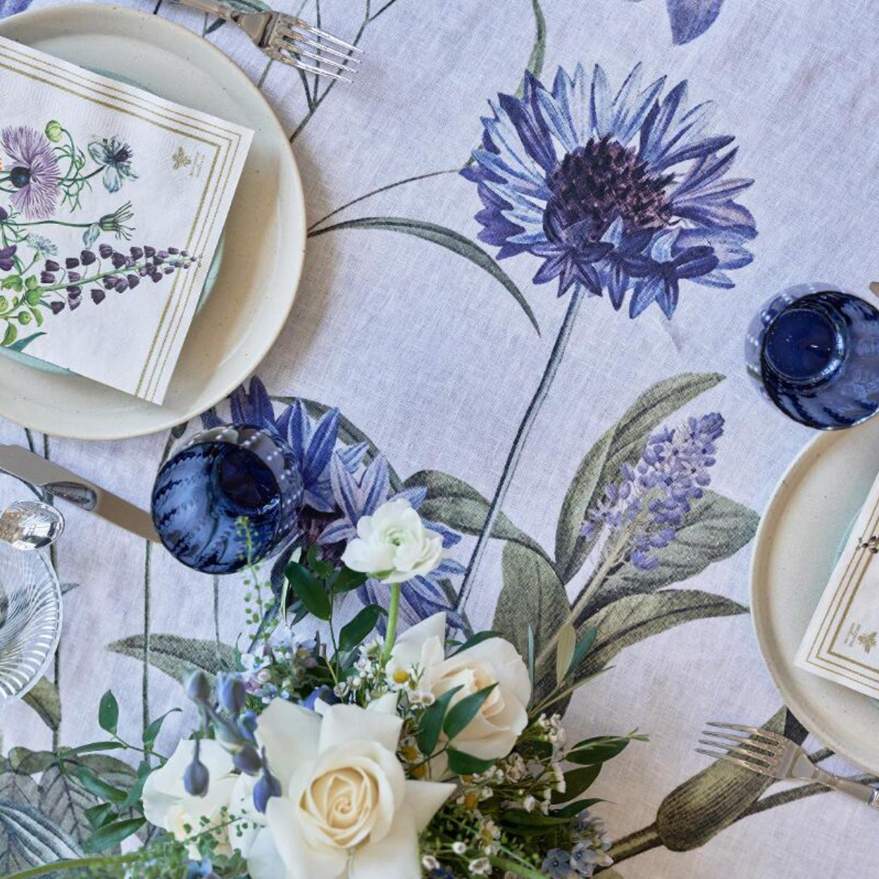 A closeup of the Blue Garden linen tablecloth, plates, and cutlery on a white background