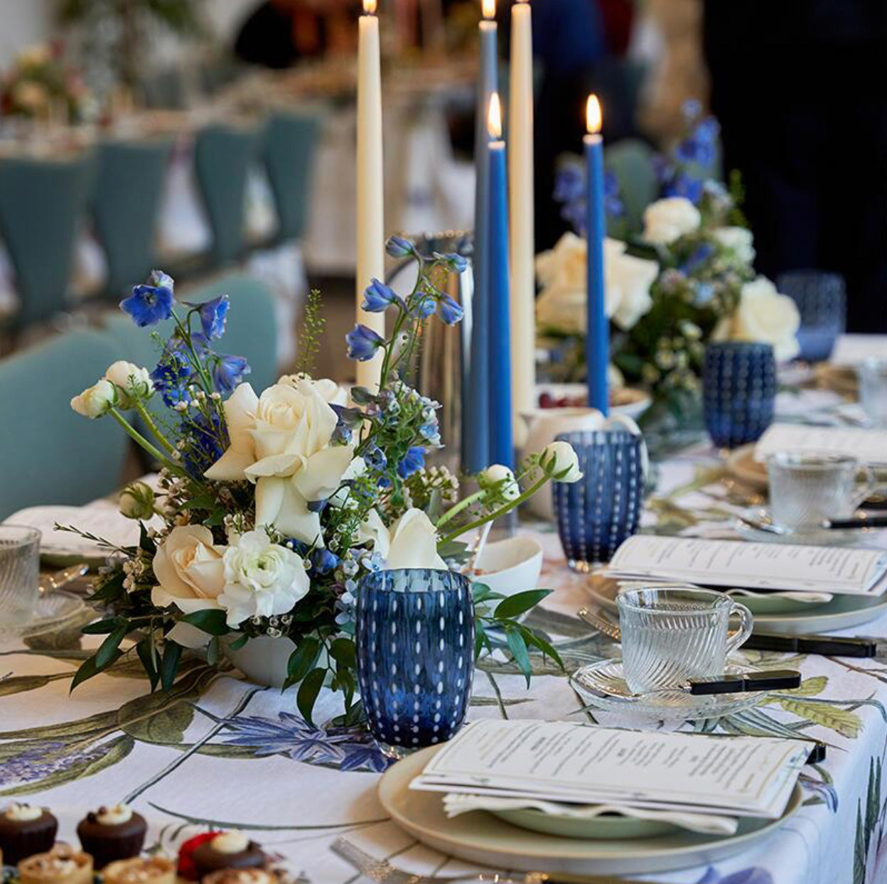 Elegant table setting with blue and white floral arrangements, candles, and blue mugs.