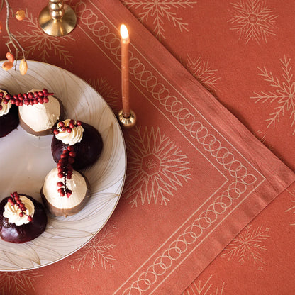 A close up of a Ciel Étoilé French cotton jacquard tablecloth and placemat featuring snowflakes in gold.