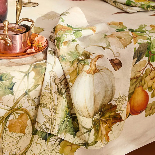 Decorative tablecloth and napkin with an autumnal design featuring pumpkins, leaves, and fruits.