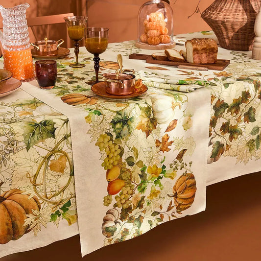 An autumn-themed cotton-linen table runner showing a decorative repeating pattern of white and orange pumpkins with trailing grapevines on a cream background.