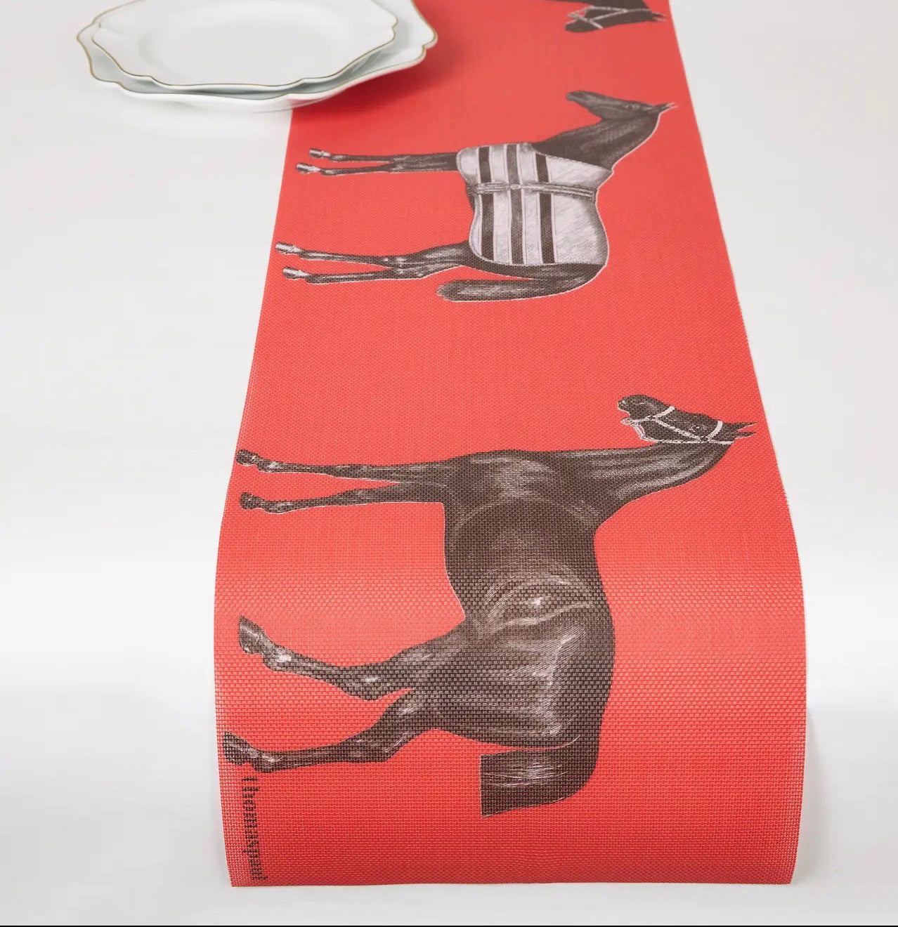Red vinyl table runner with brown horse illustrations on a white surface