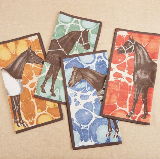 Set of four Horse Marble cotton dinner napkins arranged on a neutral fabric background. Each square napkin features a unique, elegantly illustrated brown horse motif set against a vibrant, marbled background pattern in shades of yellow gold, green, red, and blue, all finished with a crisp, dark brown piped edge.