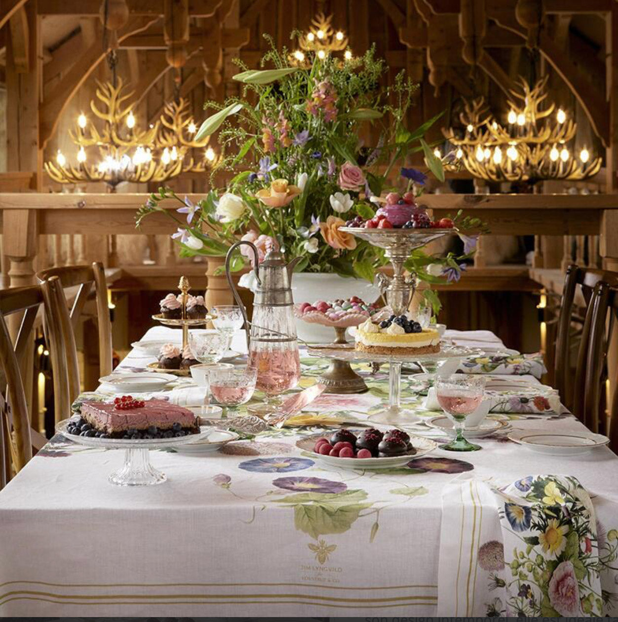 Decorative table setting with flowers, desserts, and the Flower Garden linen tablecloth in a warm-toned, wooden room.