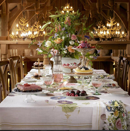 Decorative table setting with flowers, desserts, and the Flower Garden linen tablecloth in a warm-toned, wooden room.