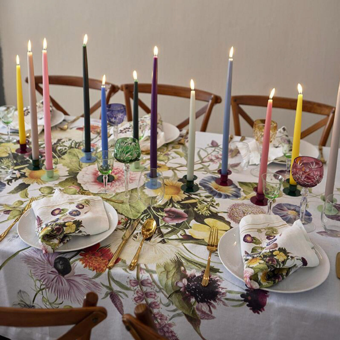 Dining table set with floral tablecloth, colorful candles, and patterned napkins.