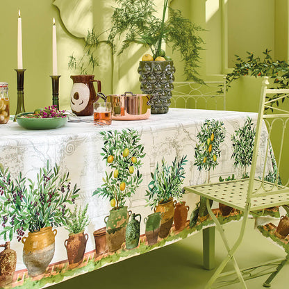 Jardin Provencal Olive Tablecloth made with cotton-linen blend covers a dining table featuring potted plants, candles, and a vase.