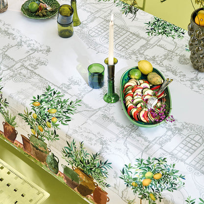 Jardin Provencal Olive Tablecloth with garden-themed design featuring a hand sketch of a French village and potted plants underneath lemons on a table setting.