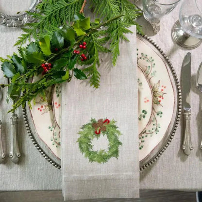 Linen napkin with an embroidered juniper wreath styled on a Christmas table setting with greenery.