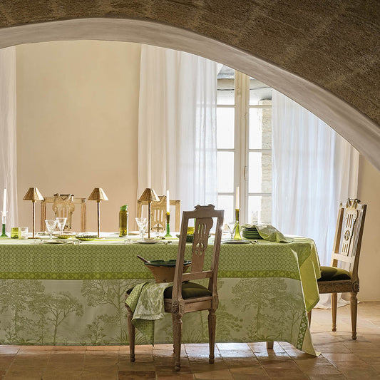 Le Sud Vert Jacquard Tablecloth in green cotton featuring a tree motif, styled on a dining table inside a rustic stone-arched room.