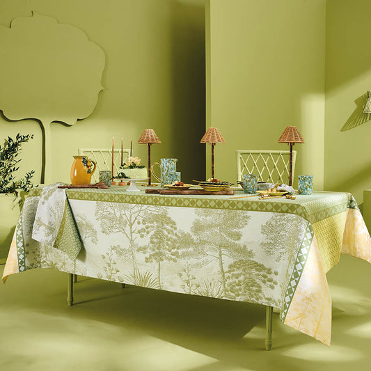 Le Sud Vert Jacquard Tablecloth in green cotton featuring a tree motif, styled on a dining table in a lime green room with coordinated table settings, lamps, and mustard yellow water vase.