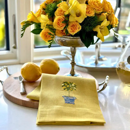 Yellow embroidered lemon topiary linen towel styled on a kitchen counter with yellow roses and fresh lemons.