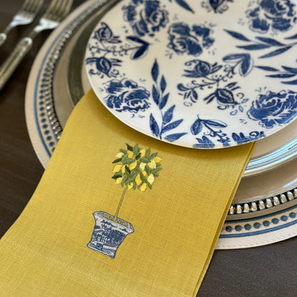 Yellow embroidered lemon topiary linen towel styled in between a stack of plates.