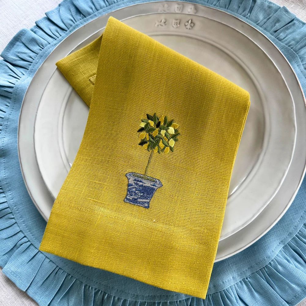 Yellow embroidered lemon topiary linen towel styled on a white plate and powder blue placemat.
