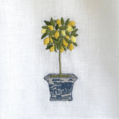 Embroidered design of a potted plant with lemons on a white linen towel.
