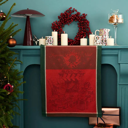 Decorative red and green dishtowel with woven Joyeux Noel and Christmas-themed elements on a teal fireplace.
