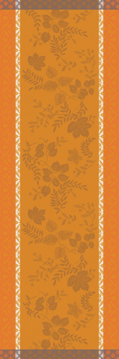 A rectangular table runner with an orange and mustard floral pattern, bordered by white floral motifs and gray decorative bands at the top and bottom.