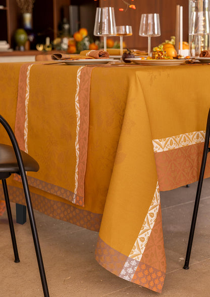 Close-up view of the Manor Lane tablecloth in mustard yellow, showing the woven Jacquard border detail, mitered corners, and rich fabric texture.