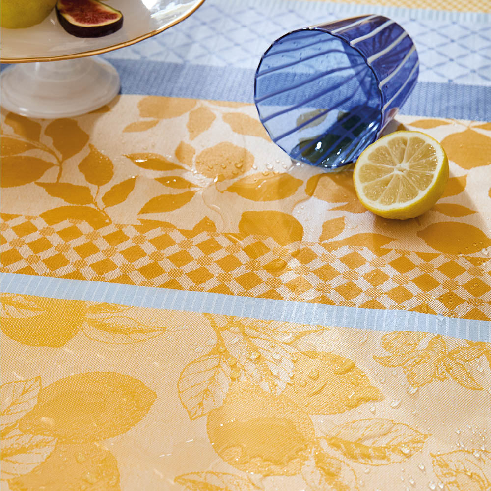 Close-up of a spilled liquid on the Mille Citrons Provence Jacquard Tablecloth in stripes of blue and yellow stain-resistant cotton with lemon motifs.