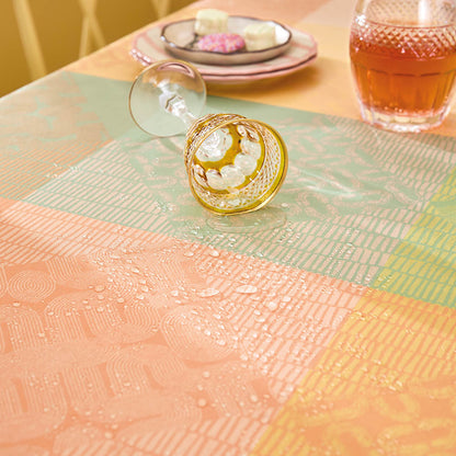 Close up of the Mille Empreintes Jacquard Tablecloth in pastel plaids of cotton with a wine glass spilling liquid on the coated, stain-resistant surface. 