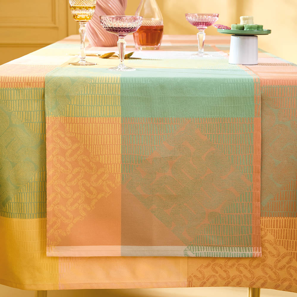 Mille Empreintes Pastel Jacquard Table Runner in pastel cotton featuring geometric, plaid-inspired motifs, draped over a dining table in a yellow-walled room.