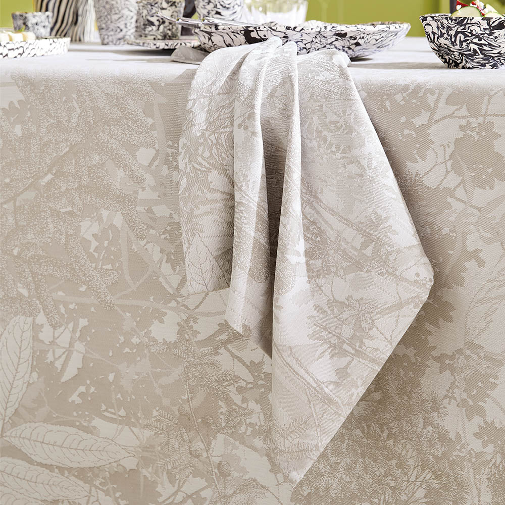 Mille Esprit Jardins Napkin in a cream botanical floral cotton jacquard draped elegantly across a matching tablecloth. 