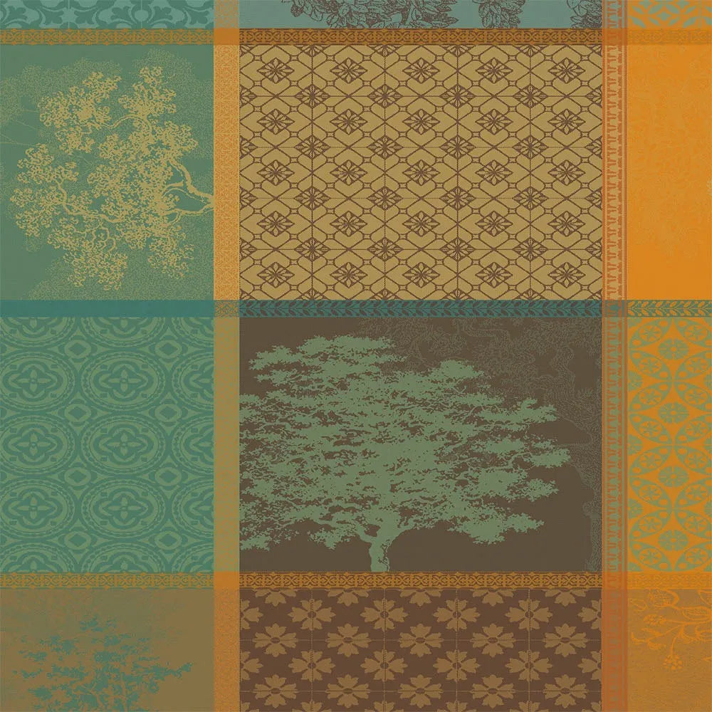 A woven cotton jacquard napkin featuring an autumnal patchwork layout of geometric squares and rectangular panels, filled with detailed evergreen tree motifs and intricate patterns in shades of orange, teal, and amber.