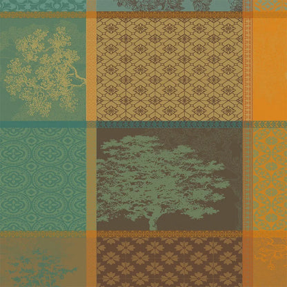 A woven cotton jacquard napkin featuring an autumnal patchwork layout of geometric squares and rectangular panels, filled with detailed evergreen tree motifs and intricate patterns in shades of orange, teal, and amber.