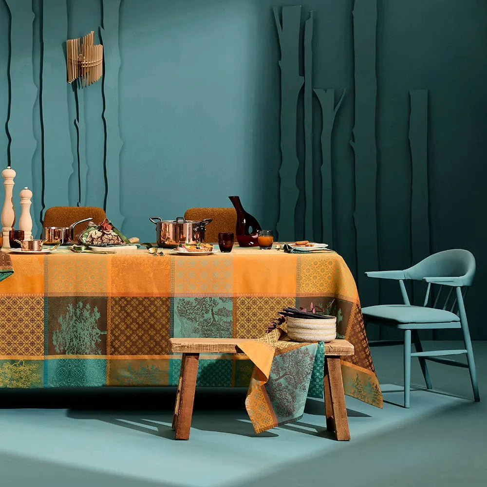 An autumnal patchwork-style checkered tablecloth dressed on a long dining table, showcased in a modern room with a deep teal background.