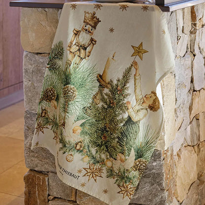 A cotton-linen kitchen towel with a vintage "Noel Vintage Doré" holiday design draped over a rustic stone pillar. The print features a classic wooden nutcracker, a child placing a golden star on a Christmas tree, lit candles, pine cones, and scattered gold stars.