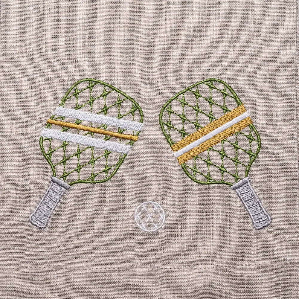 Embroidered pickleball rackets and a ball on a flax linen fabric background.