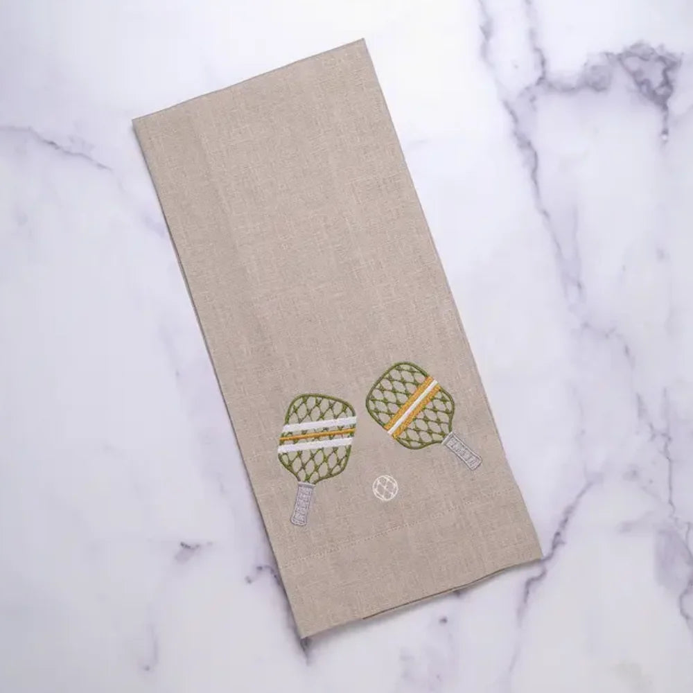 Embroidered pickleball rackets and a ball on flax linen towel laying  on marble.