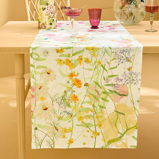 Rosee Du Matin Printemps Table Runner featuring pink and green watercolor floral print on cotton-linen blend draping elegantly across a yelow table set with rose colored glassware and a floral pitcher.