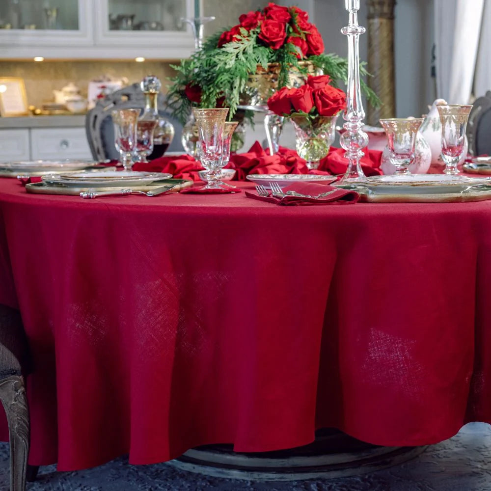 Red round 100% linen tablecloth draped on a dining table set for a holiday dinner.