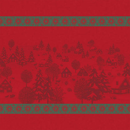 Full view of a red Sous Les Étoiles French cotton jacquard napkin featuring illustrations of a winter village and snowflakes in green trim.