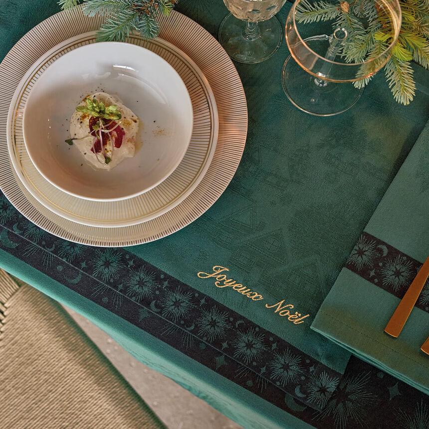 Green Sous Les Étoiles French cotton placemat with gold Joyeux Noël script styled on a holiday dining table.