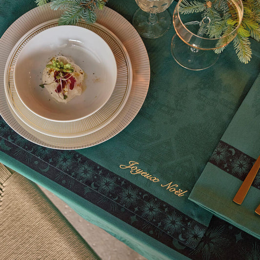 Green Sous Les Étoiles French cotton placemat with gold Joyeux Noël script styled on a holiday dining table.