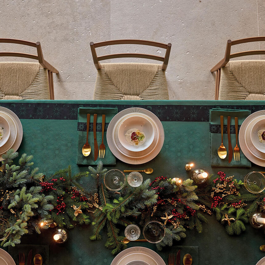 Aerial view of the green Sous Les Étoiles French cotton jacquard tablecloth draped on a dining table set with Christmas tree branch centerpieces. 