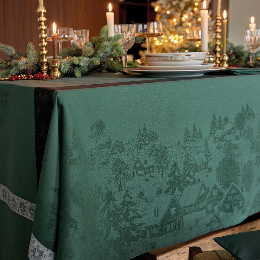Dark green cotton jacquard tablecloth featuring a woven winter landscape pattern of trees, stars, and villages along the drop.