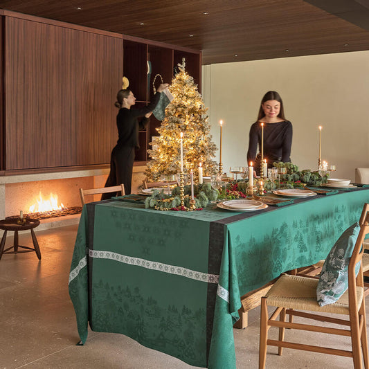 Green Sous Les Étoiles French jacquard tablecloth styled on a festive holiday dining table with lit candles and a Christmas tree.