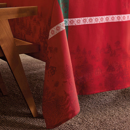 Close-up of red Sous Les Étoiles jacquard tablecloth featuring intricate holiday village design. 