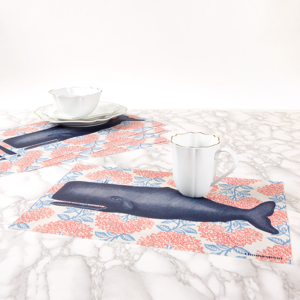 Whale-themed vinyl placemats and white teacups on a marble table top.