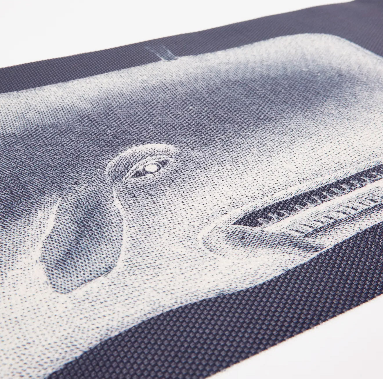 A detailed, close-up view of a gray woven vinyl table runner featuring a large, hand-screened illustration of a majestic whale tail on a classic basketweave texture.